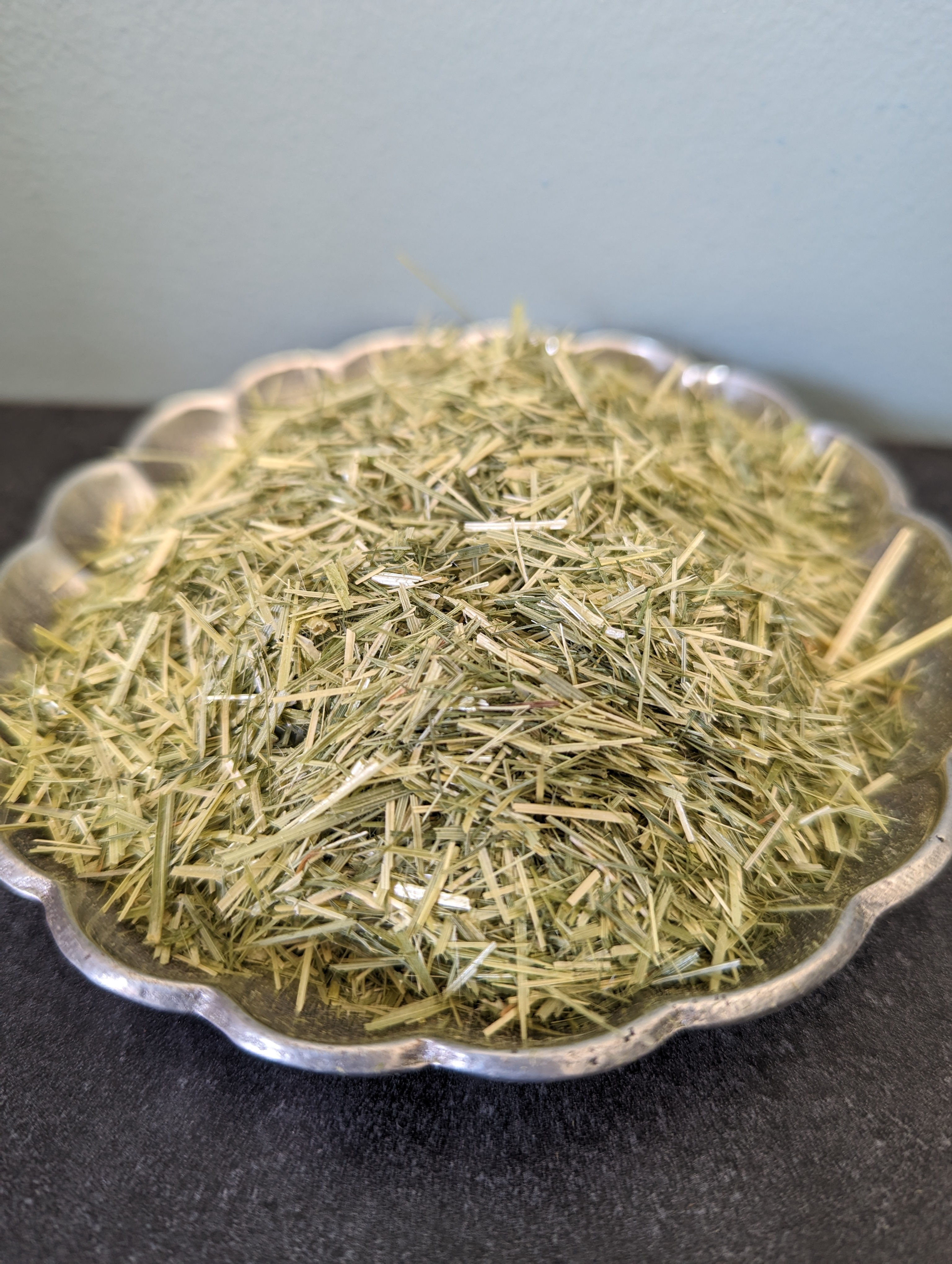 Dried green herbs in a decorative silver scalloped bowl.