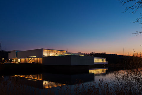 Complexe aquatique « Les Bains du Lac » à Soissons illuminé au crépuscule. Photo prise par Julien Loize, photographe d'architecture et immobilier en Picardie et Paris, expert en mise en valeur des bâtiments modernes et des paysages environnants. Reflets lumineux sur l'eau accentuant le design épuré de l'édifice.