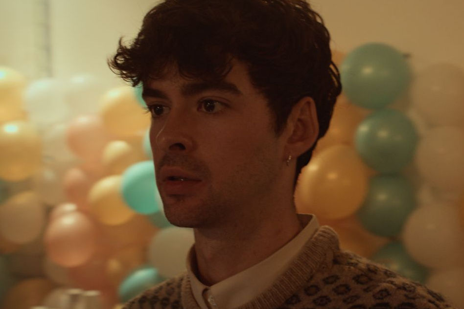 Man with curly hair at a party with pastel balloons