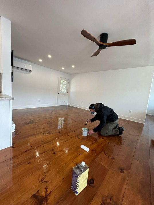Person varnishing wooden floor in empty room.