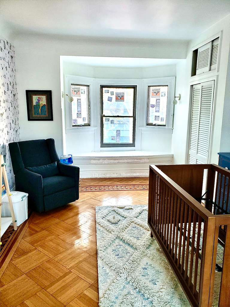 Bright room with armchair, crib, and large window.