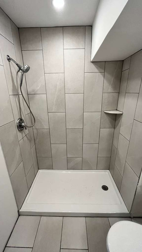 Small, tiled shower with wall-mounted showerhead.