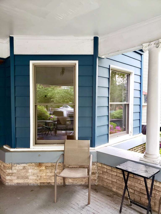 Blue house exterior with windows and a porch chair.