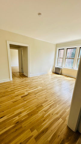 Bright, empty room with wooden floor and large windows.