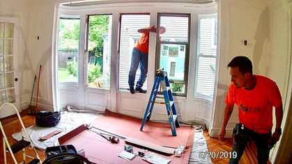 Person installing window, standing on a ladder indoors.