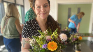 A woman holding a bouquet with daisies and chrysanthemums at a flower arranging workshop.