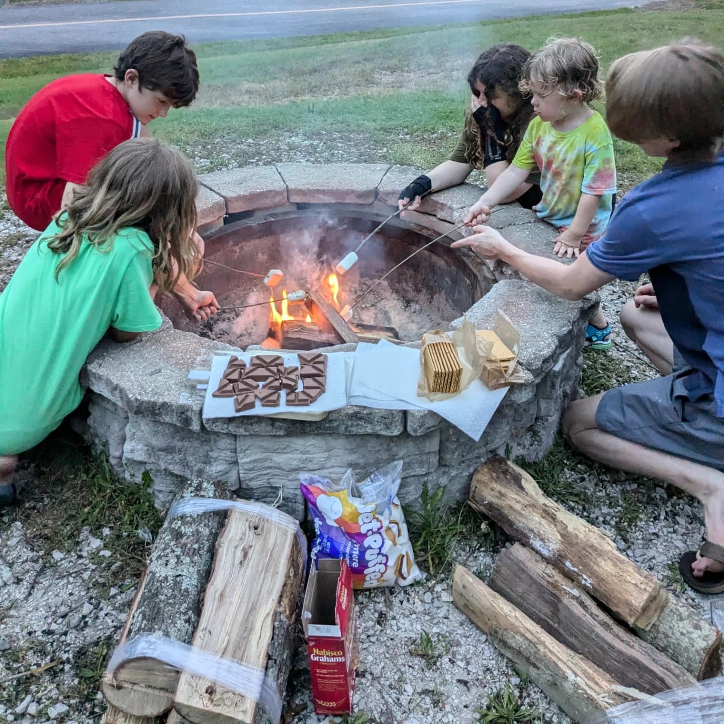 Kids making s’mores around a backyard fire pit on a summer evening.