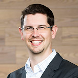 Brian Oblinger, headshot, dark short hair with glasses. A white button up shirt and black blazer