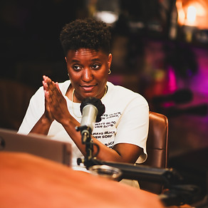 Shana Sumers, Black Woman with short haircut, wearing a cream shirt speaking into a microphone, hands together