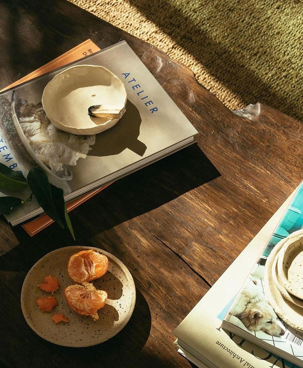 Wooden table with a peeled tangerine on a speckled plate, magazines and a cozy, sunlit atmosphere.