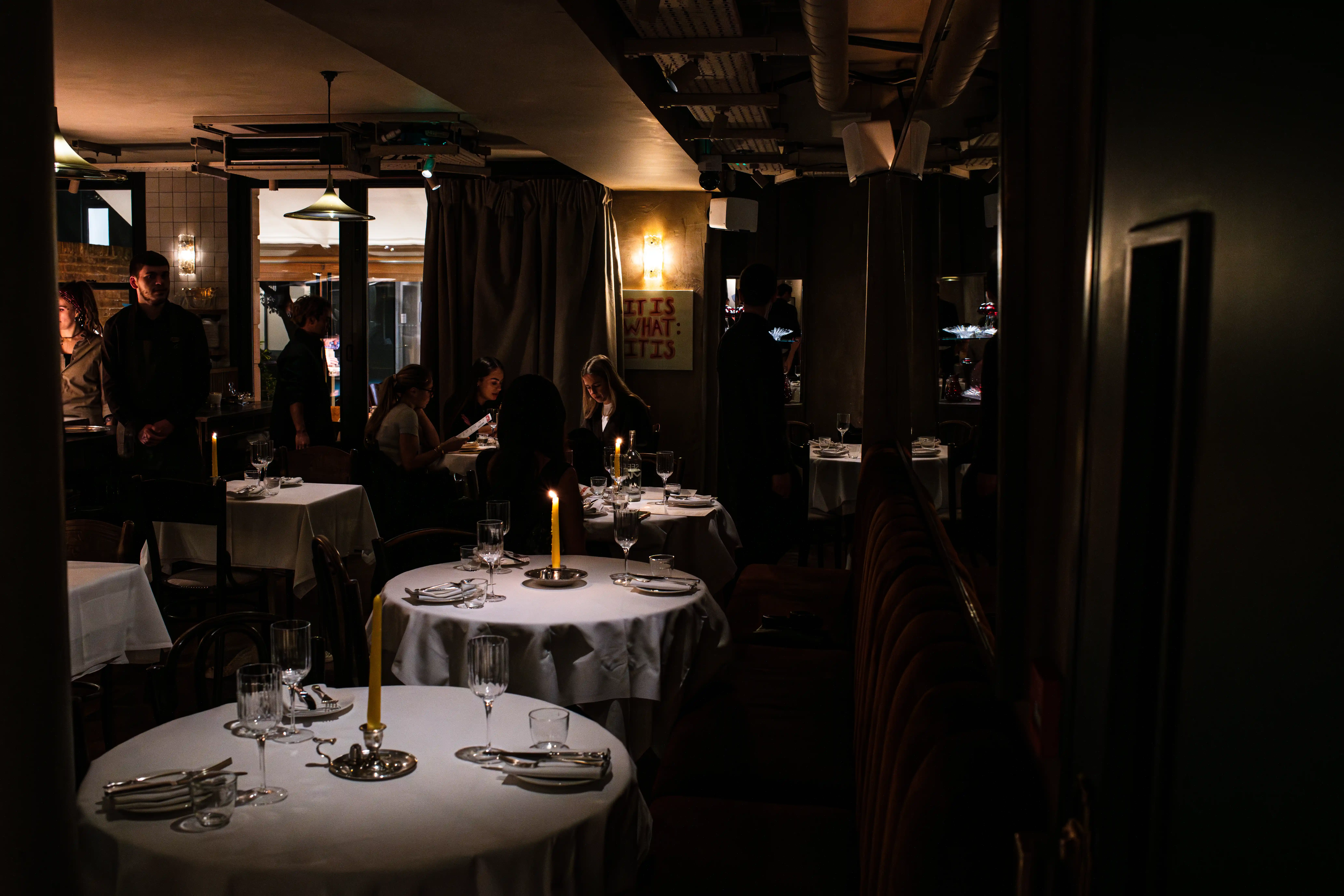 A dark intimate restaurant with candle lit tables and an open kitchen 