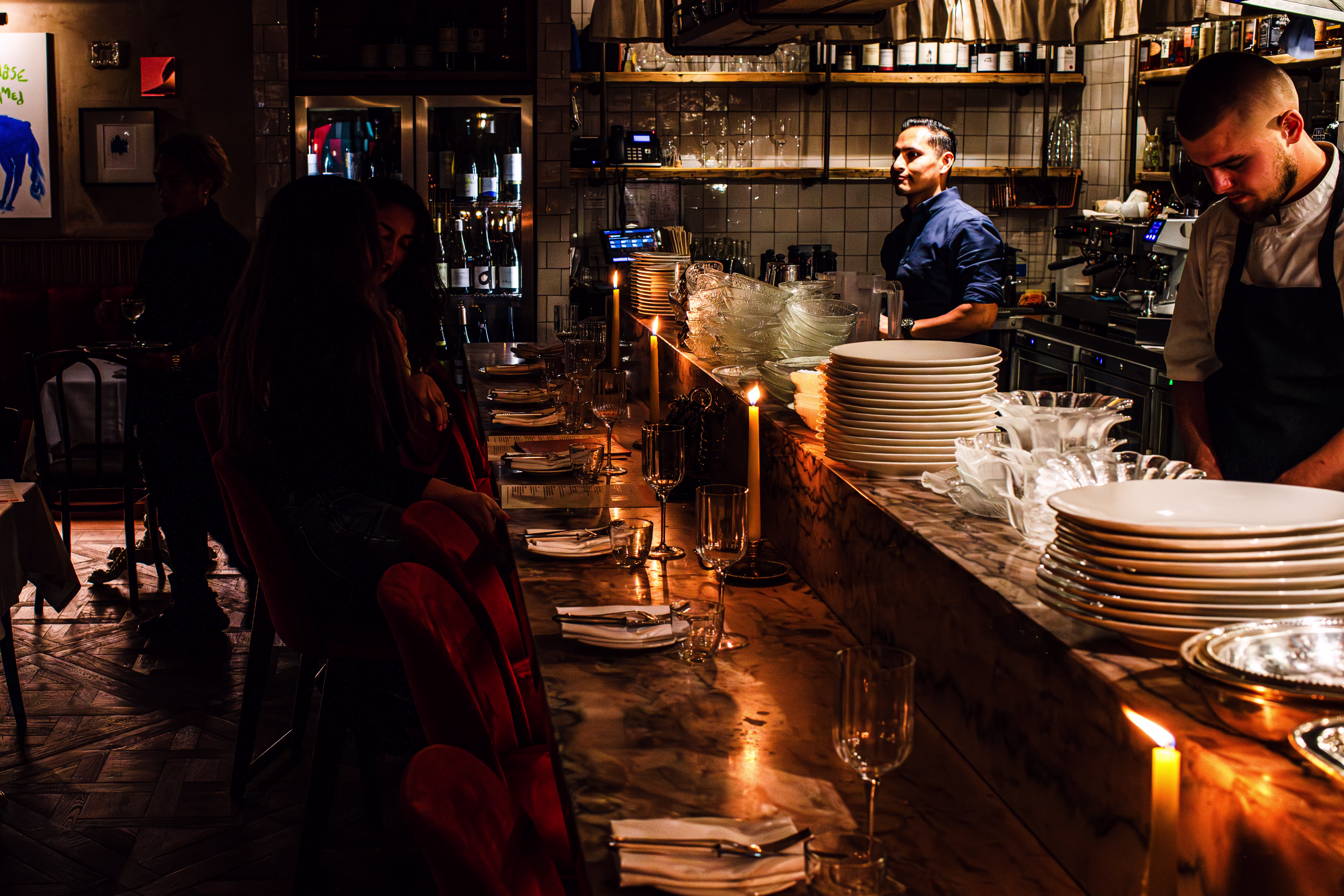 A dark intimate restaurant with candle lit tables and an open kitchen 