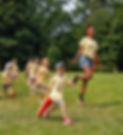 A female counselor skipping on the grass, leading six campers