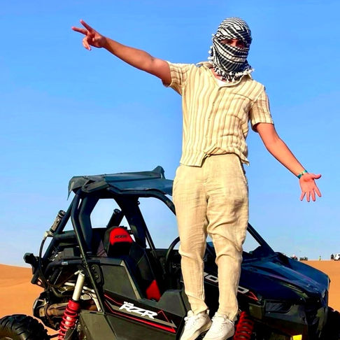 Man posing near buggy in desert with blue sky and DUBAI DOO