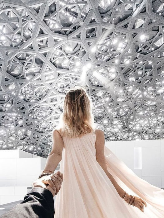 Woman in dress leads by hand under a stunning, intricate architectural dome, at Louvre Ahu Dhabi