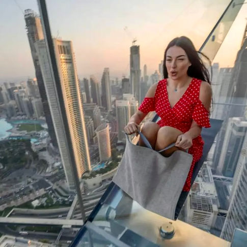 Woman in red dress standing on a glass floor, skyline view. DUBAI DOO