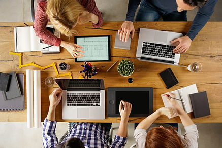 Four professionals sitting around a table with their computers, notes, and devices, showing an example of how IronBridge Private Wealth partners with CPAs and legal counsel to coordinate the client's financial plan.