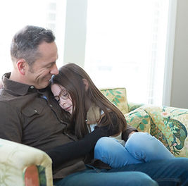 dad and his little girl snuggle on living room sofa of their South Jordan, Utah home