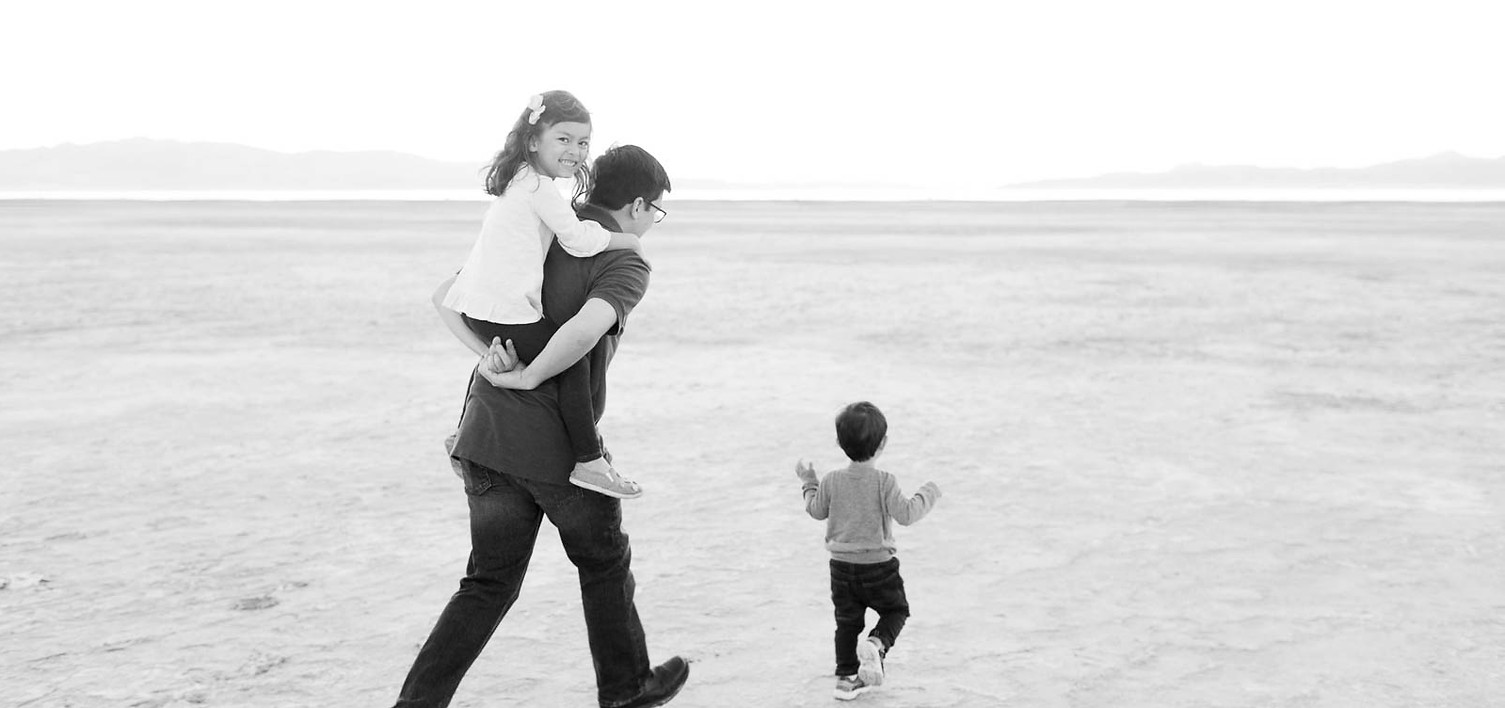little girl rides piggy back on her dad while they chase her little brother in a beautiful Salt Lake Valley, utah location