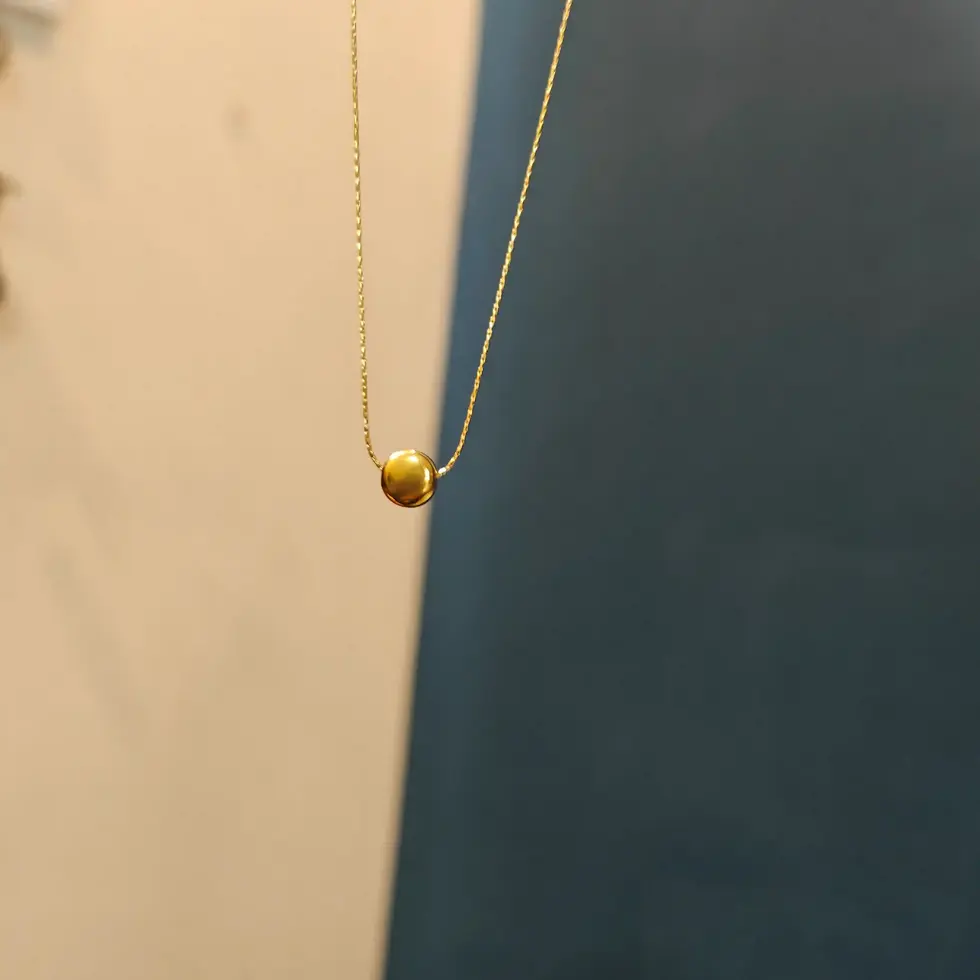 Gold-toned minimalist necklace with a small round polished pendant on a delicate chain.