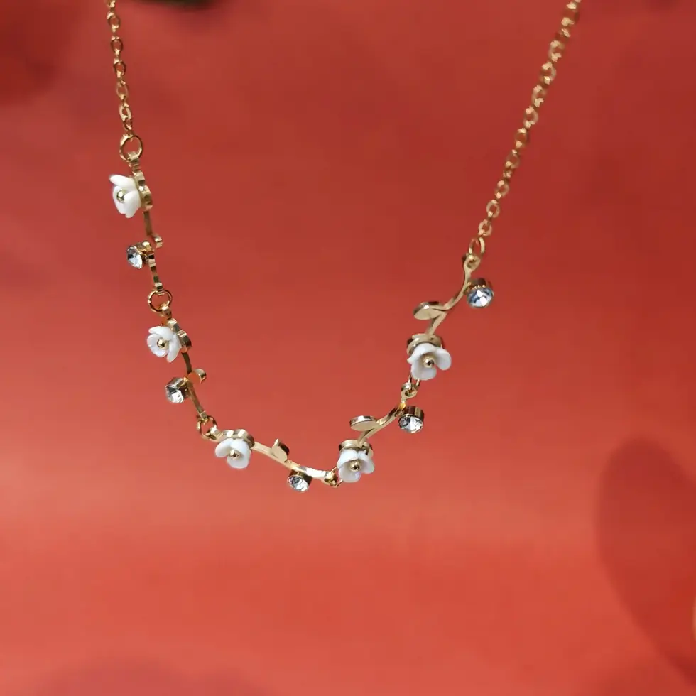 Elegant gold floral necklace featuring white enamel flower details and sparkling crystal stones arranged on a delicate chain.