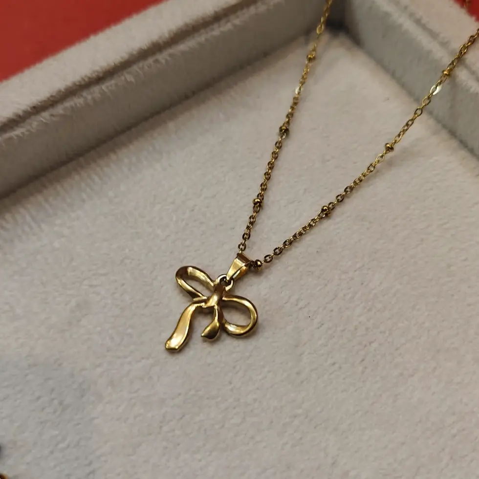 Delicate gold necklace featuring a tiny bow-shaped pendant on a fine minimalist gold chain.