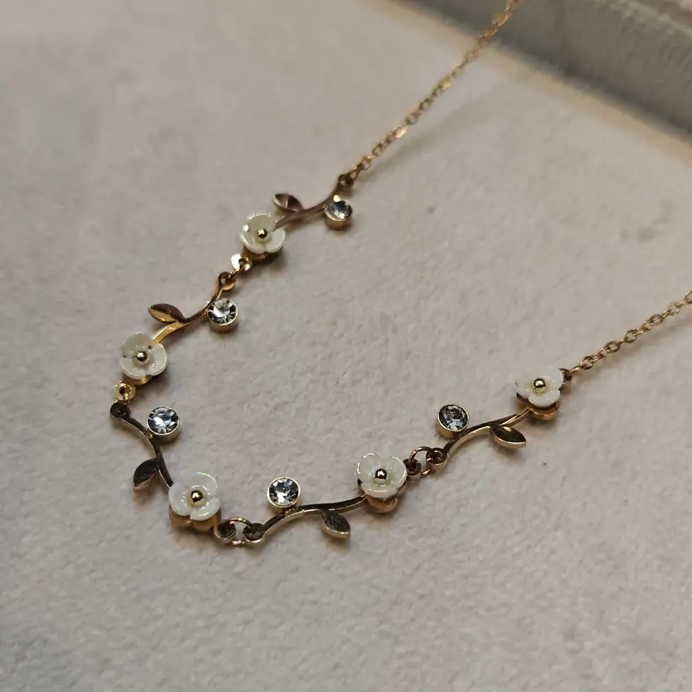 Elegant gold floral necklace featuring white enamel flower details and sparkling crystal stones arranged on a delicate chain.