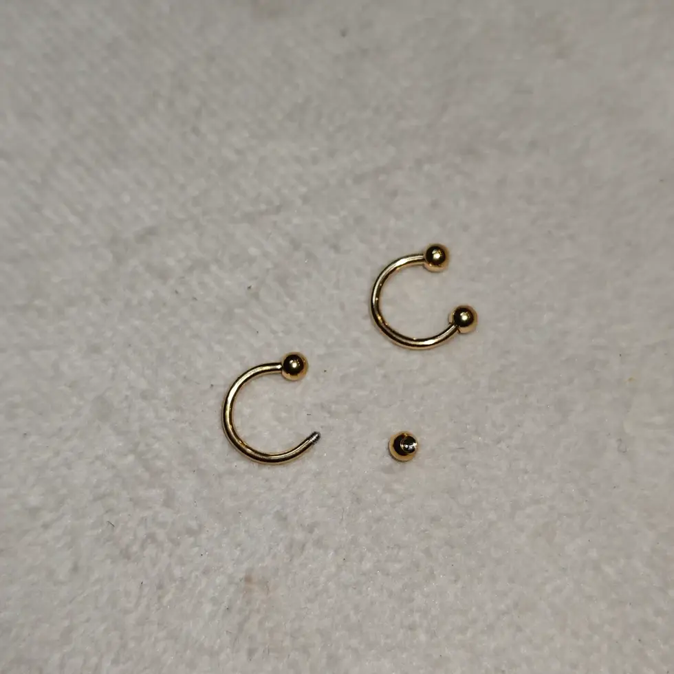 Gold-tone men's hoop earring with ball-end accents on a neutral background.