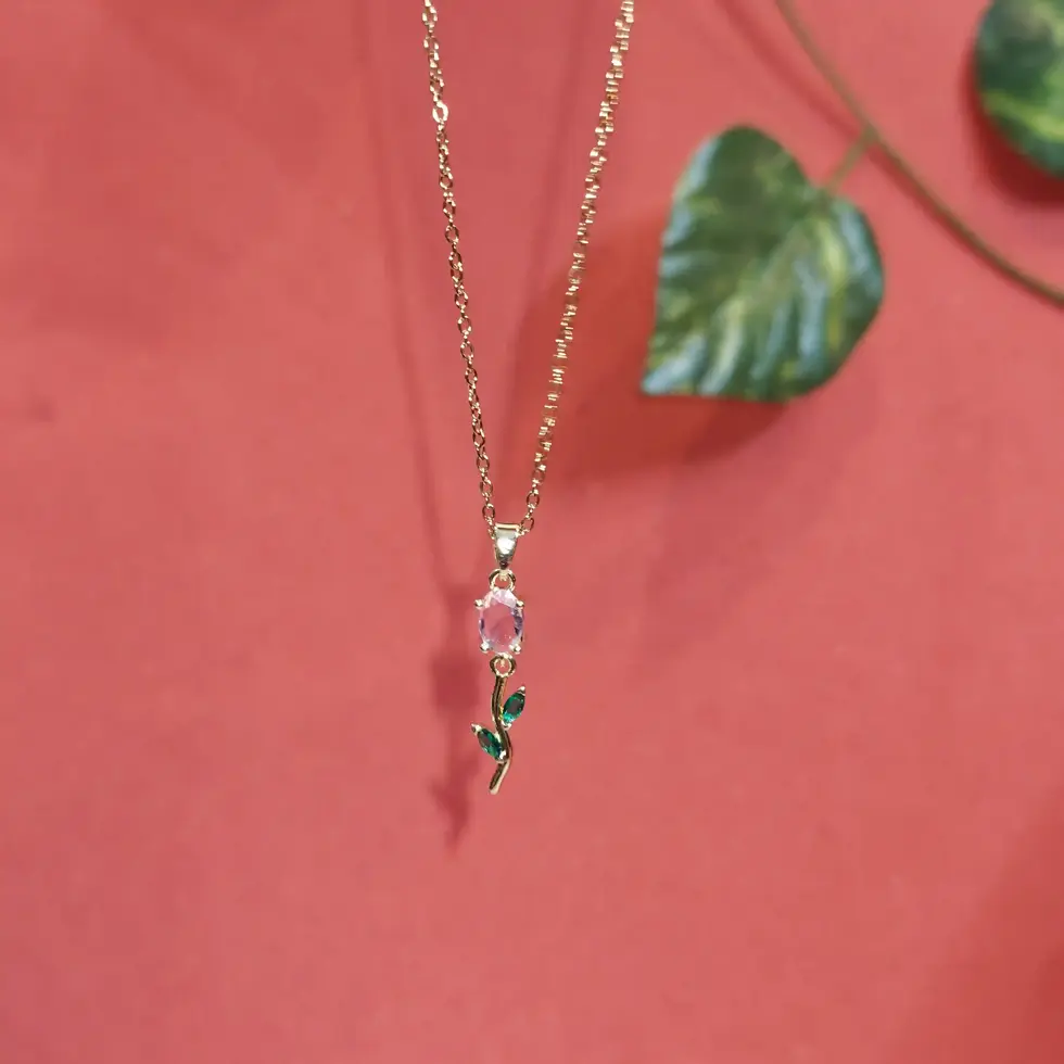 Elegant gold necklace featuring a delicate blush crystal floral pendant with emerald green leaf accents on a fine chain.