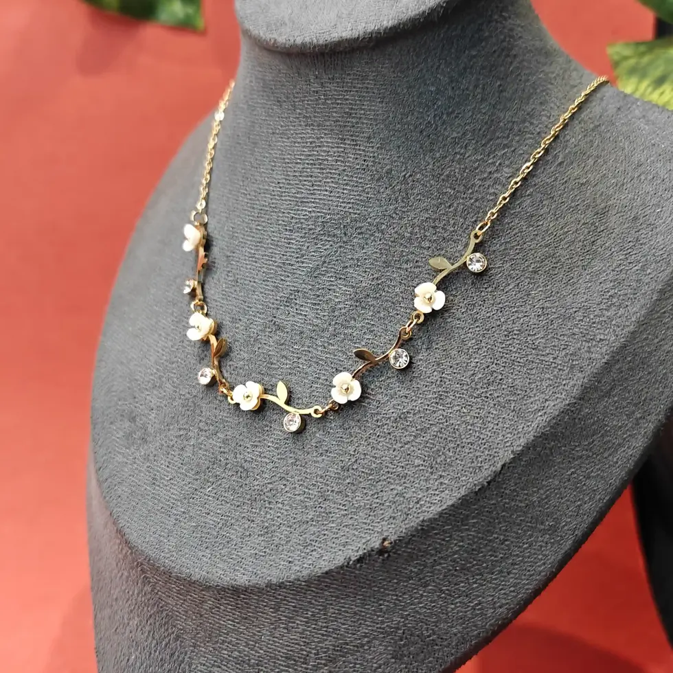 Elegant gold floral necklace featuring white enamel flower details and sparkling crystal stones arranged on a delicate chain.
