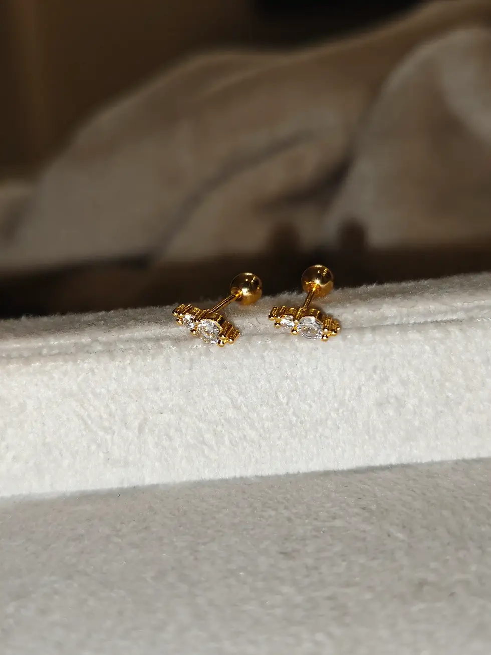 Delicate gold-plated ball-back stud earrings featuring a dainty bow-inspired design with sparkling clear stones and a minimal