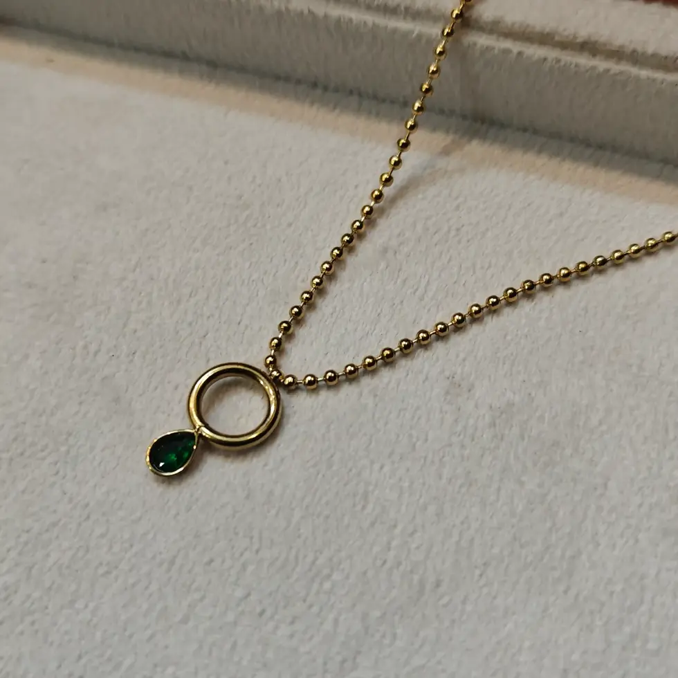 Minimal gold pendant necklace featuring a delicate circular charm with a dangling emerald green teardrop stone on a fine gold