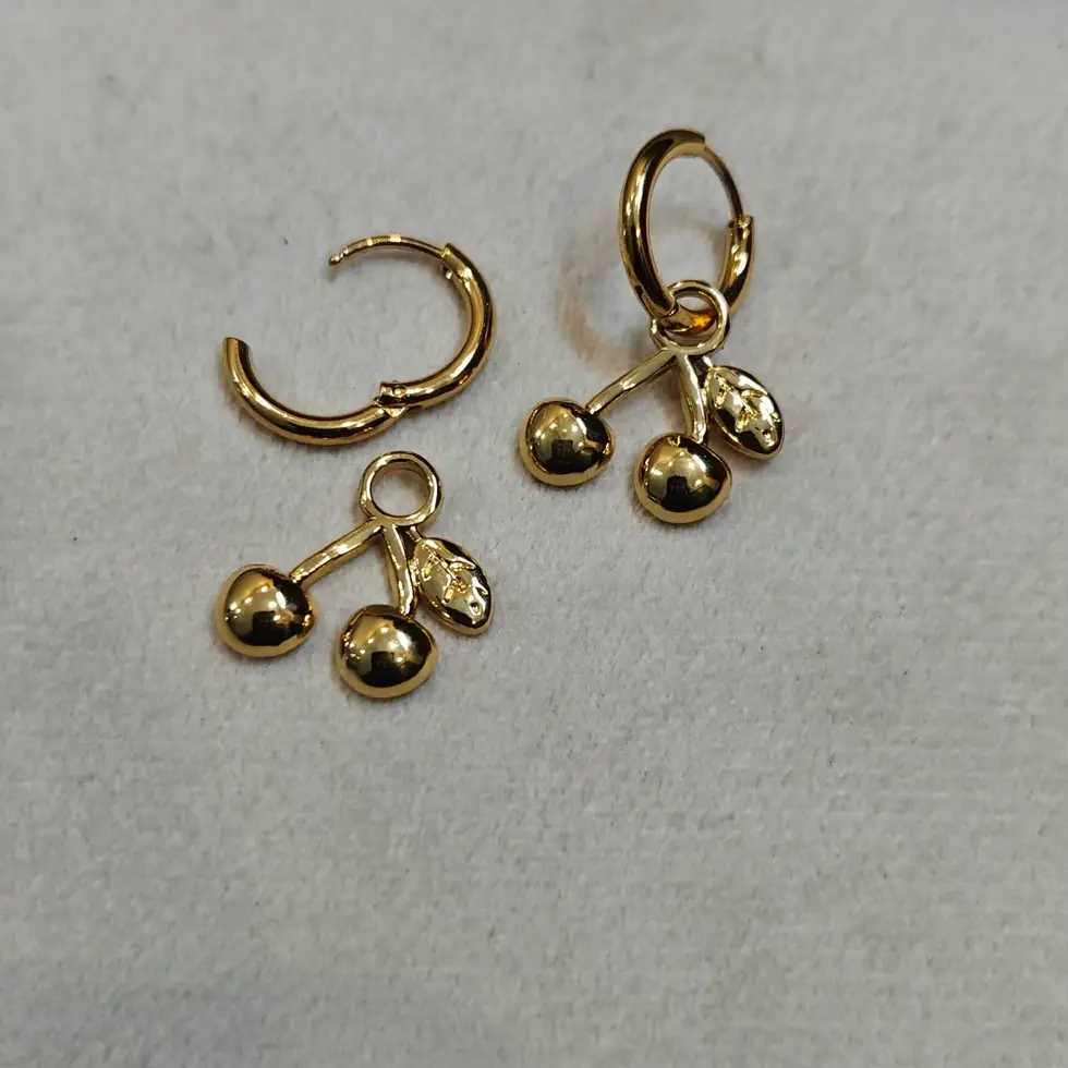 Gold-toned hoop earrings with dangling heart and leaf charms, placed on a soft surface.