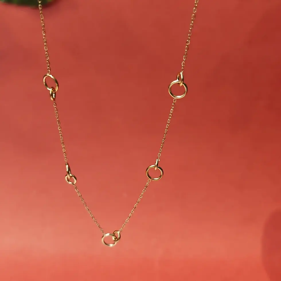 Minimal gold necklace featuring abstract circular and twisted ring charms spaced elegantly along a delicate chain.
