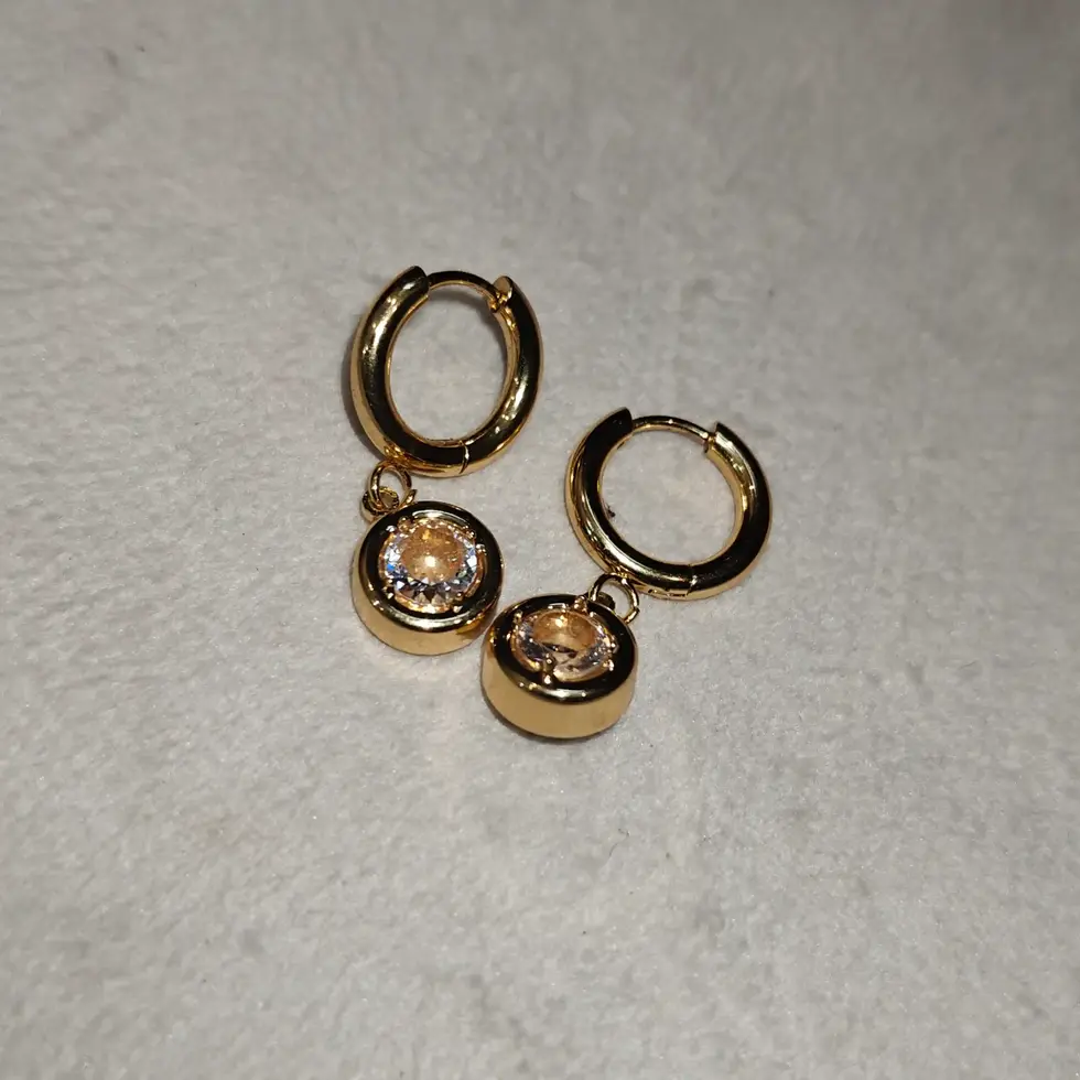 Gold-toned huggie hoop earrings with a single dangling round charm set with a white stone.