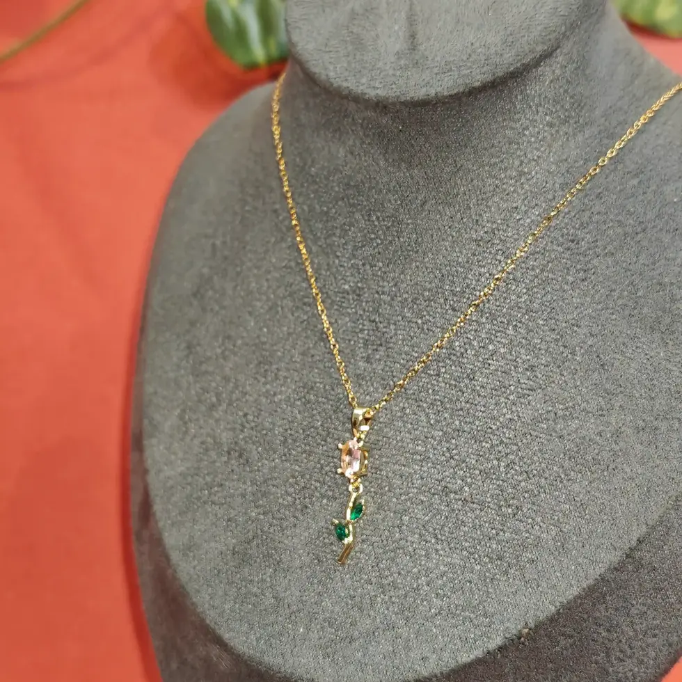 Elegant gold necklace featuring a delicate blush crystal floral pendant with emerald green leaf accents on a fine chain.