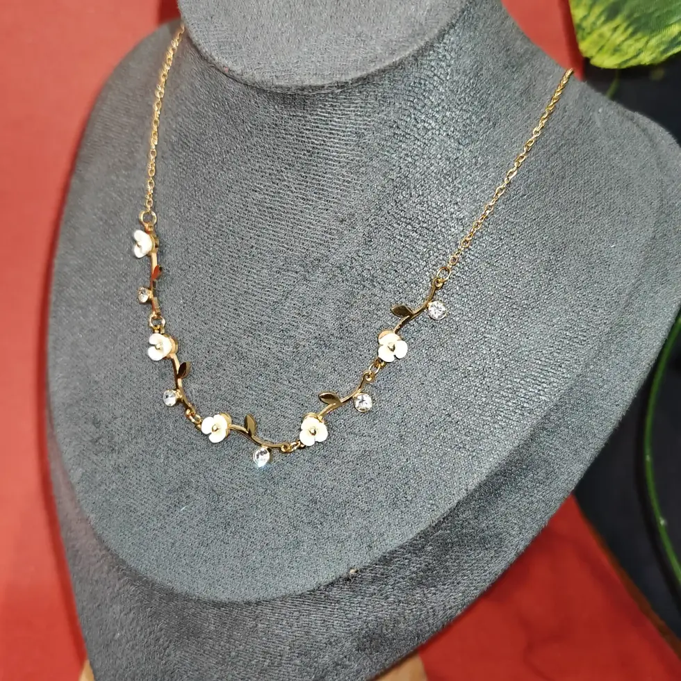 Elegant gold floral necklace featuring white enamel flower details and sparkling crystal stones arranged on a delicate chain.