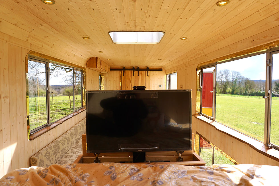 This is a view of a small living space as if you were sat on the bed. you can see a tv which has come out of the bed stand.