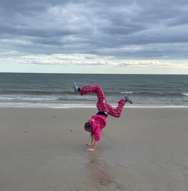 Thumbnail: Girl athlete doing gymnastics at the beach while wearing a pink Own Your Game Sweatshirts and Pink Pajama pants