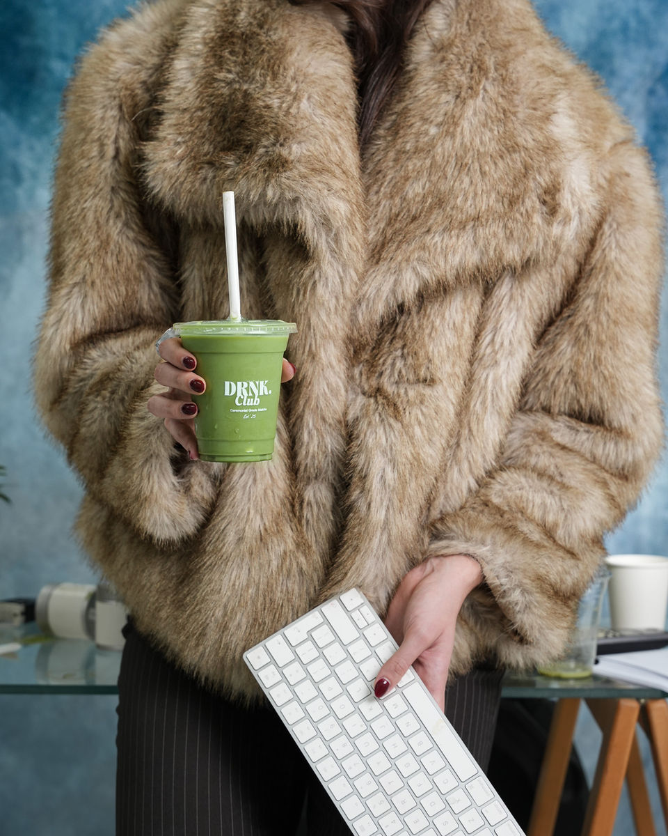 Person holding a DRNK Club ceremonial grade matcha drink while wearing a fur coat