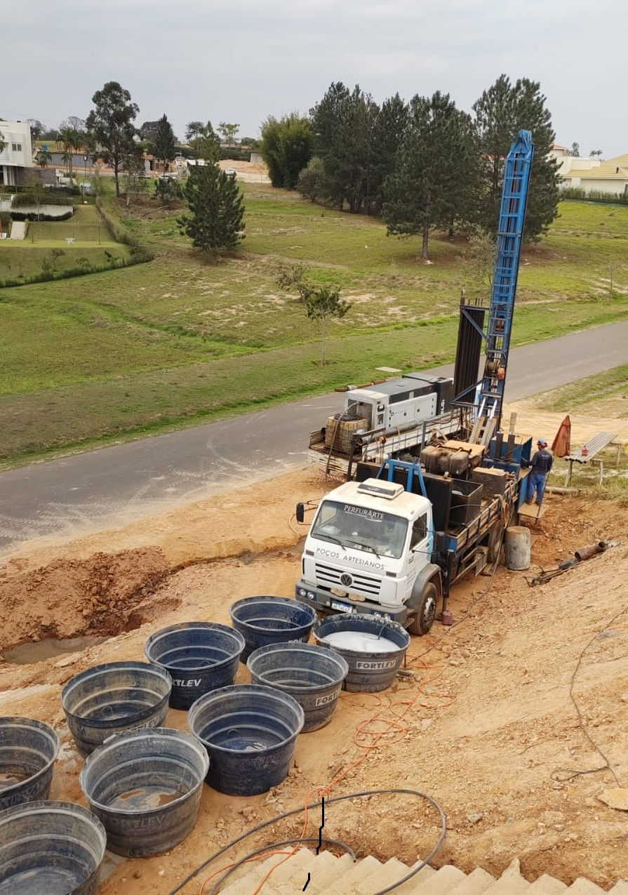 Caminhão perfuratriz da Perfurarte em paisagem verde, com reservatórios à frente. Perfure em Jundiaí-SP com a Perfurarte.