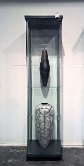 Two vases inside a glass display cabinet, black and white, against a white wall.