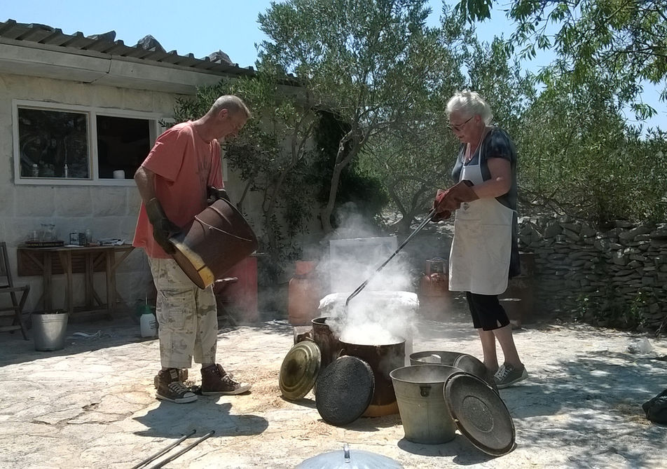 Two people raku firing over a large kiln outdoors with smoke rising.