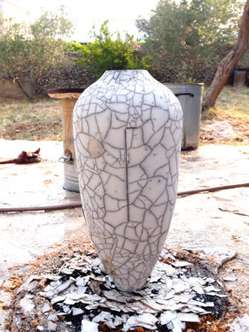 Large white vase with a cracked design, sitting outside on a stone surface.