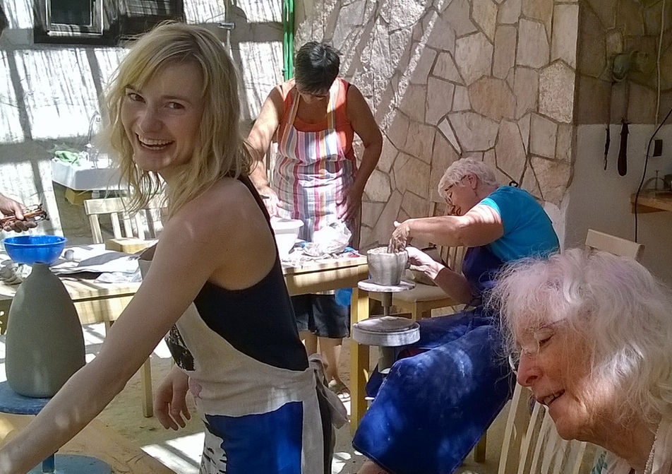 Woman smiling in pottery class with other people, crafting pottery