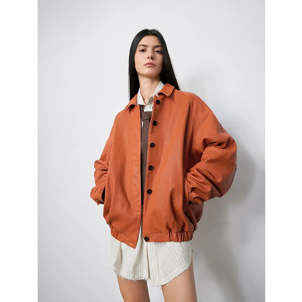 Woman in an orange jacket over a striped shirt, hands in pockets, standing against a plain white background, looking confident.