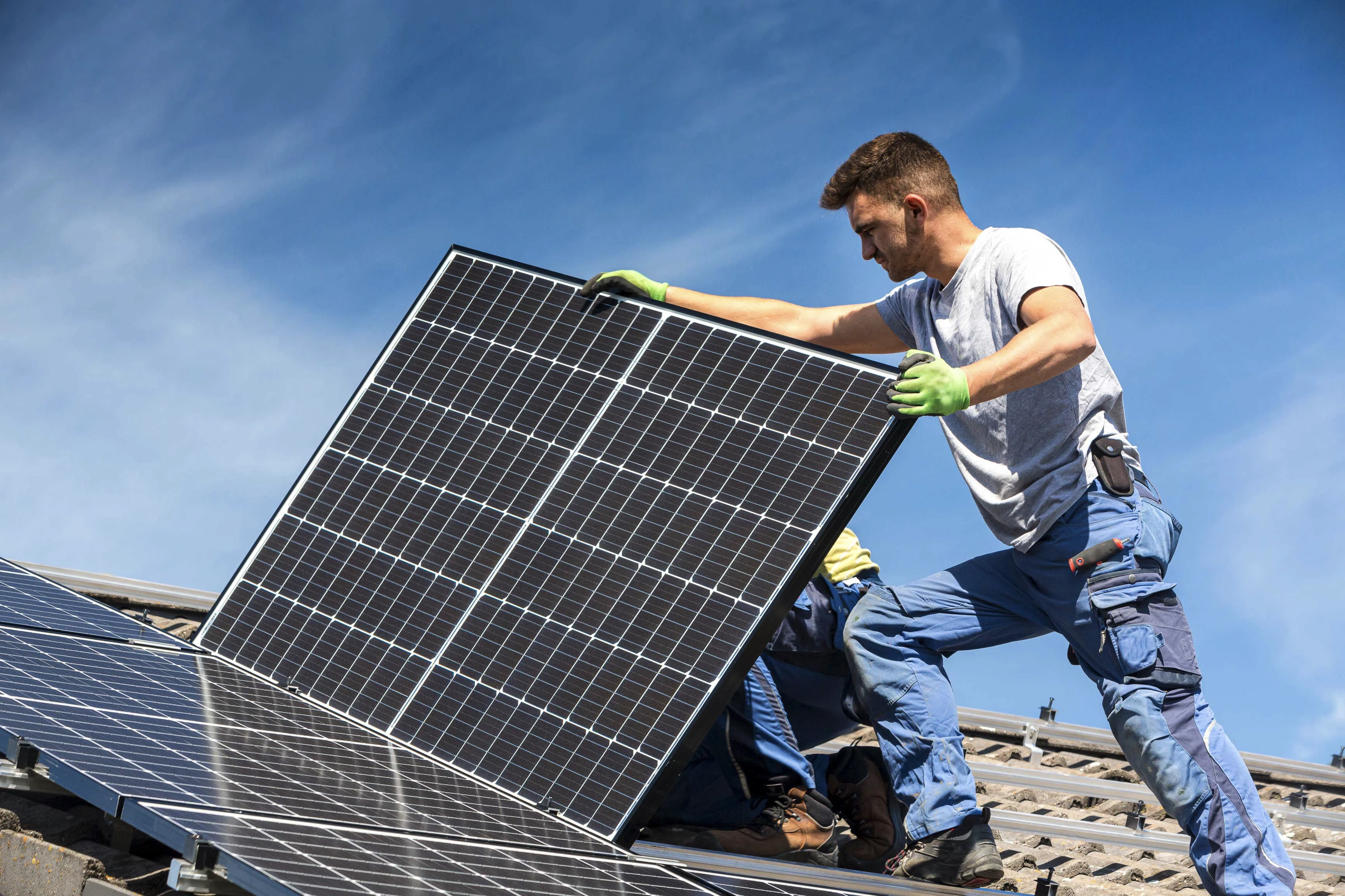 Un homme dépourvu d'équipement de protection individuelles installant un panneau solaire sur un toit en pente.