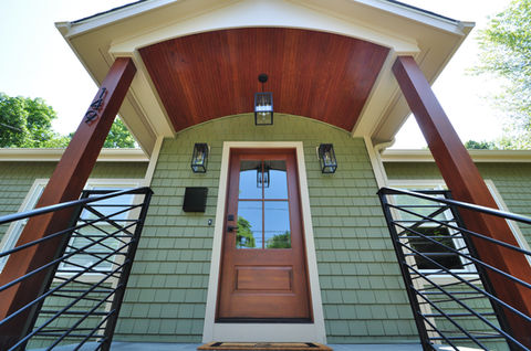 The front entrance of a home, featuring a wood-paneled ceiling, large angled wood columns, and a black metal railing.