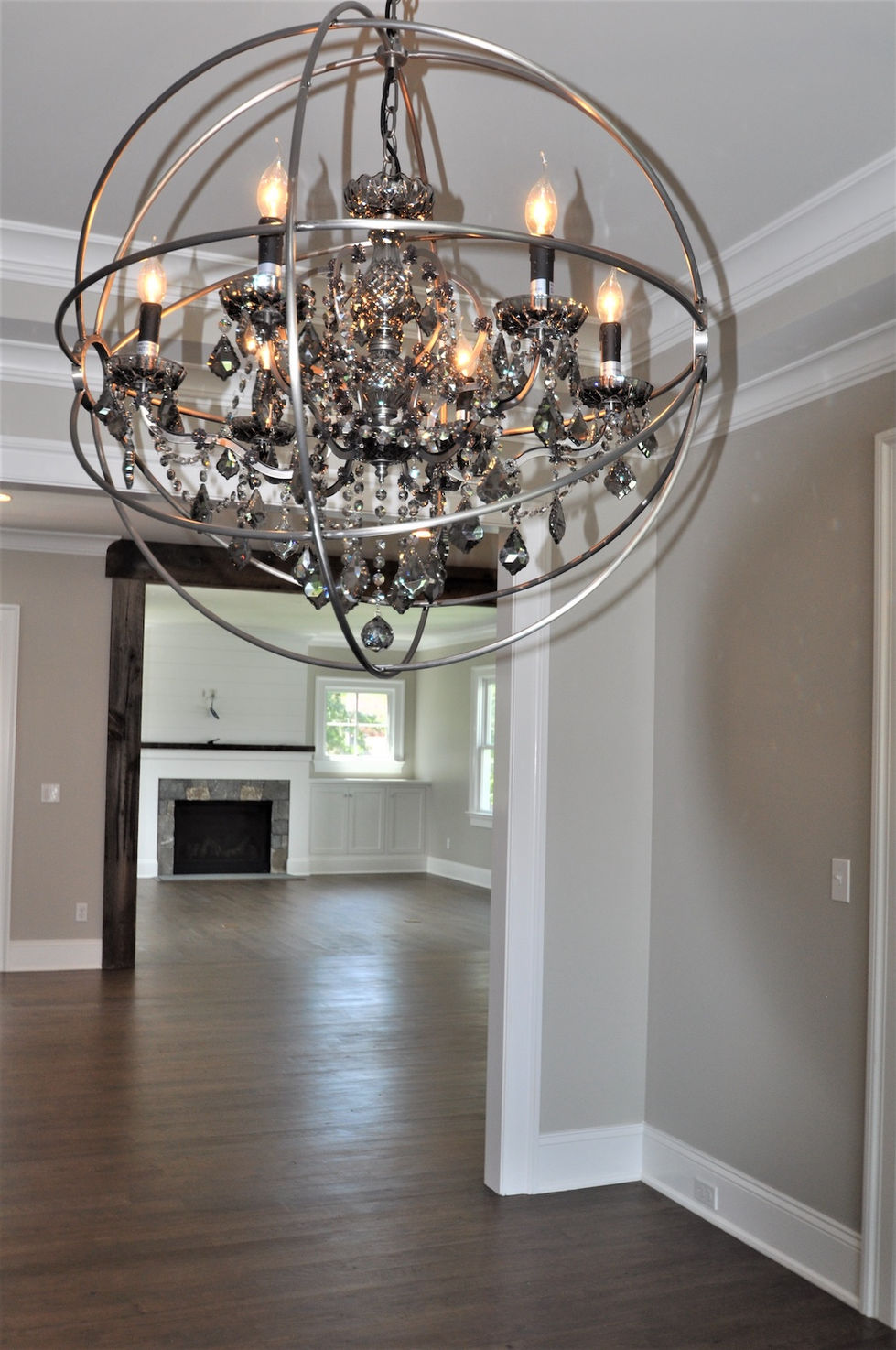 a chandelier hanging from the ceiling looking at the living room with beams