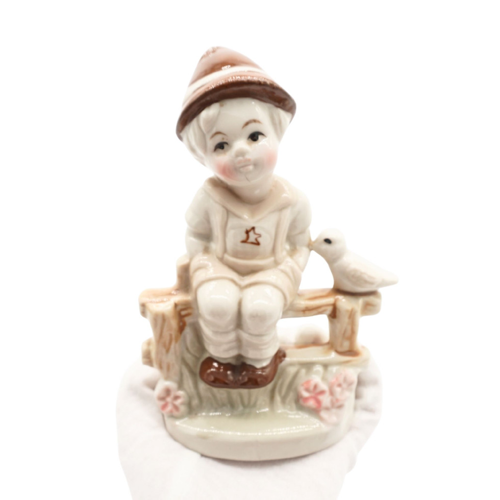 Little Boy Sitting on Wooden Fence with Bird Figurine